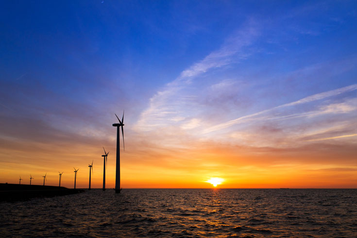 Offshore wind turbines sitting in the ocean against a golden sunset